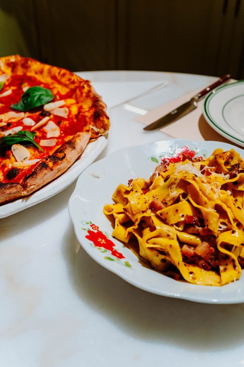 A pizza and a plate of pasta on a table
