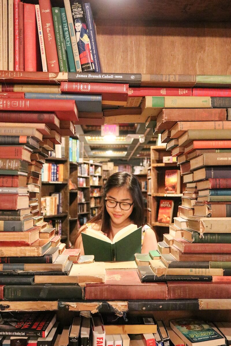 Photo by Ying Ge A woman with glasses reading a book framed by stacks of old books
